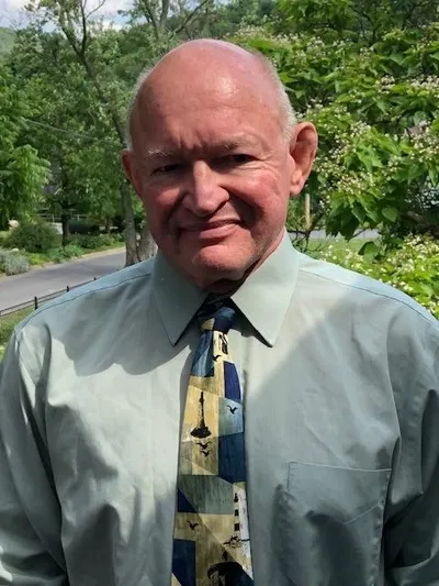 A man in a blue shirt and tie standing outside.